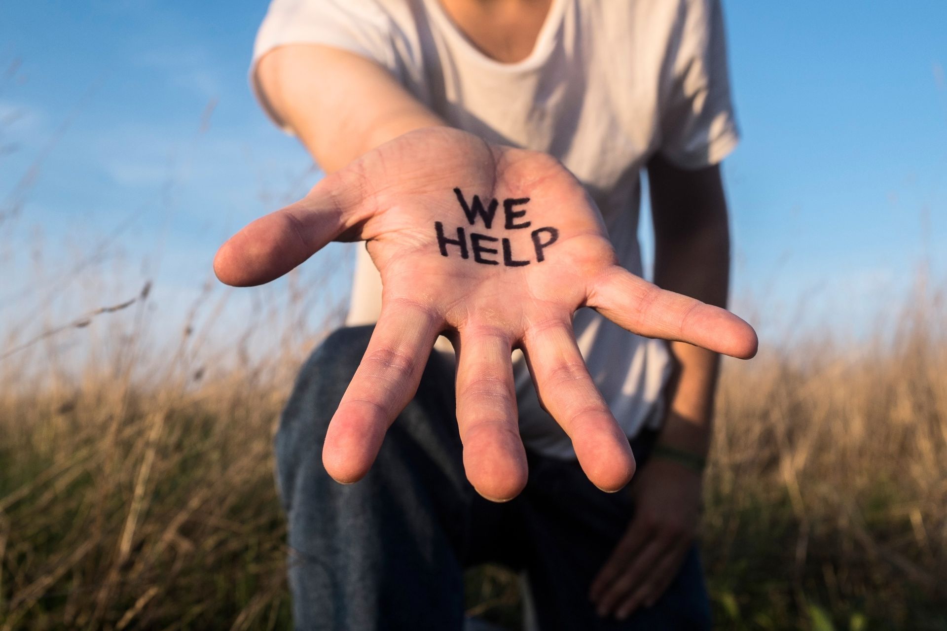 A person is holding out their hand with the words 'we help' written on it.