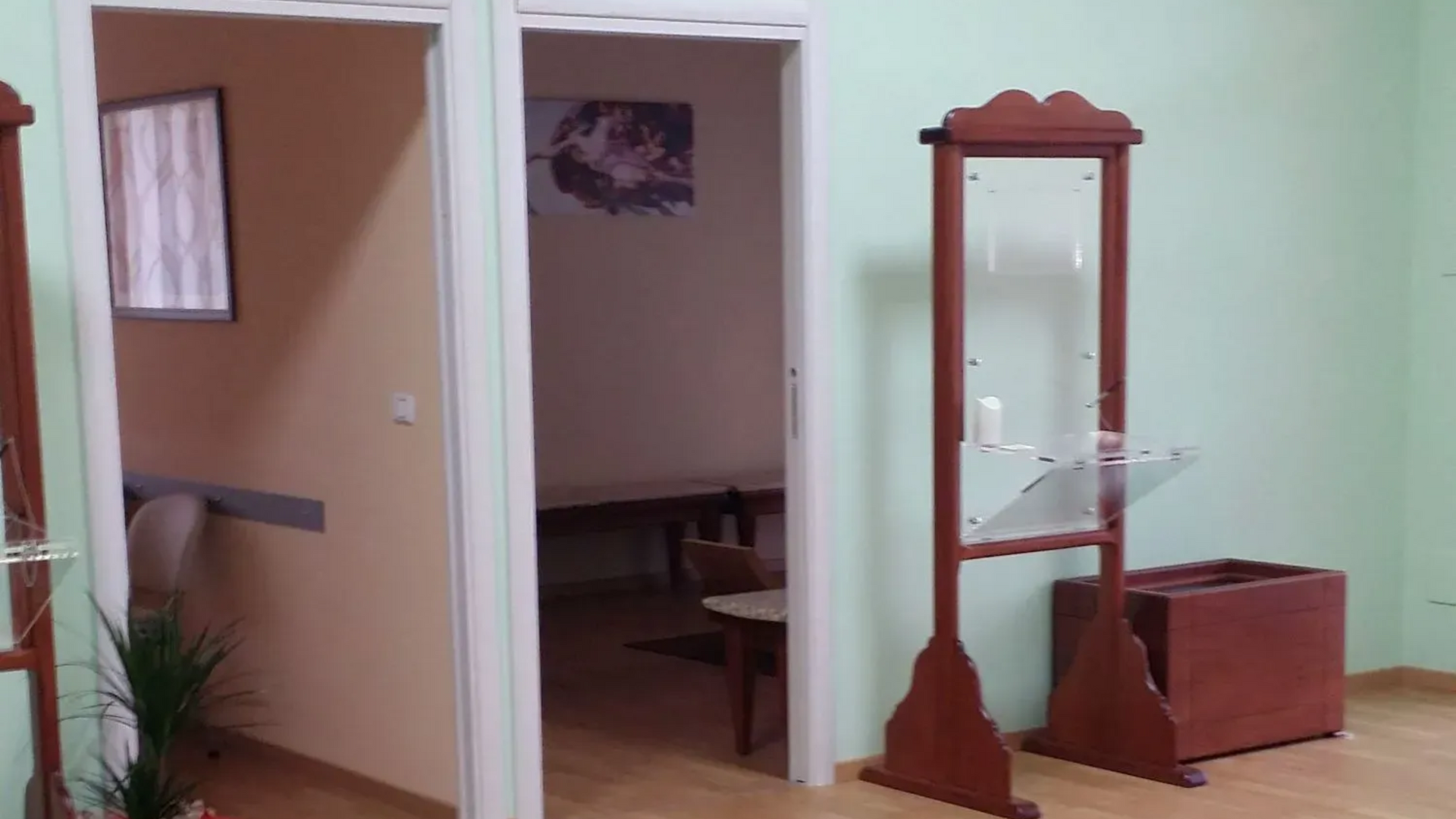 Stanza vuota con pareti verde menta, porta aperta, specchio e mobili in legno.