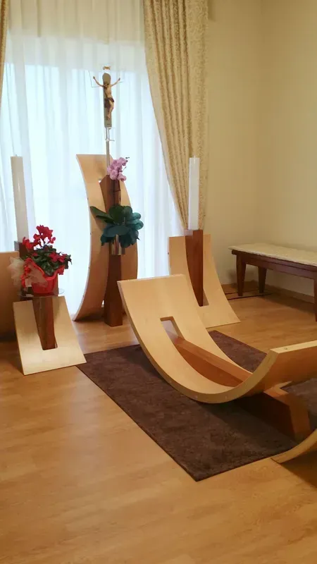 Moderna sala di meditazione con poltrone in legno, cuscini da pavimento, fiori e tende morbide.
