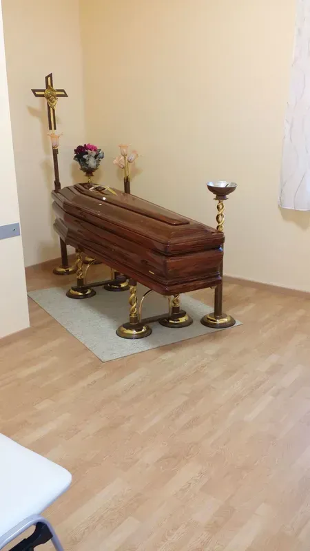 Bara di legno in una piccola cappella con candele, fiori e una croce sul muro.