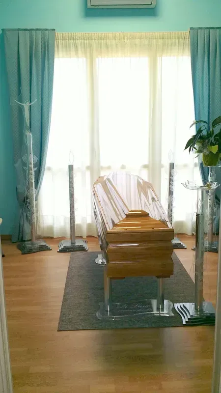 Stanza luminosa con tende color verde acqua, una finestra soleggiata e una sedia di legno su un tappeto sopra un pavimento in parquet.