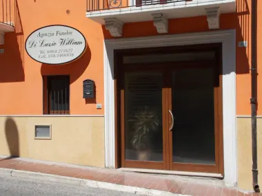 Facciata arancione dell'edificio con porta a vetri e insegna ovale sopra l'ingresso.