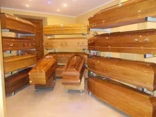 Bare di legno esposte in una sala espositiva di articoli funebri, con finiture marroni lucide e pareti color crema.