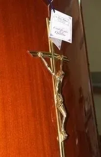 Un crocifisso appeso a una porta di legno con un piccolo biglietto bianco attaccato sopra.