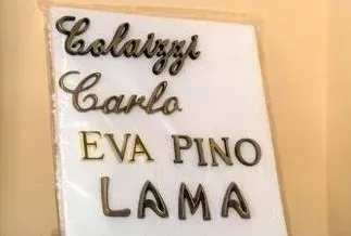 Lavagna bianca con i nomi in corsivo e stampatello in nero e oro: Caluzzi, Carlo, EVA PINO, LA MA.