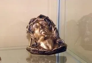Busto in bronzo raffigurante un volto femminile, esposto su una mensola di vetro.