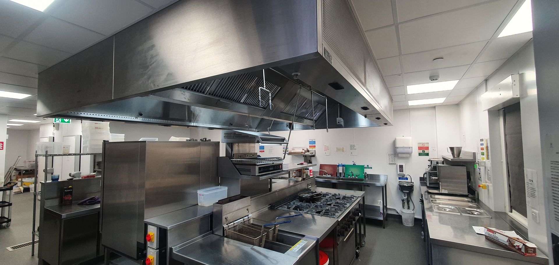Stainless-steel commercial kitchen with stovetop, hood, prep counters, and bright overhead lights.