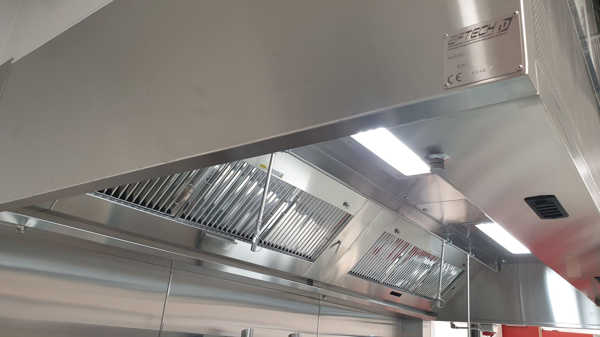 Stainless steel commercial kitchen hood with grease filters and bright overhead lights