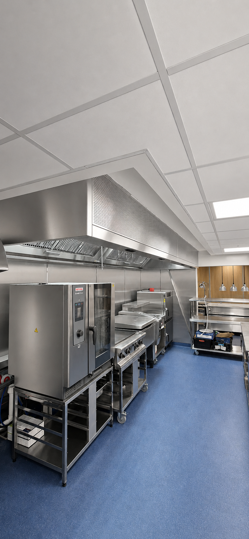 Commercial kitchen with stainless steel appliances and counters on a blue floor under bright ceiling lights