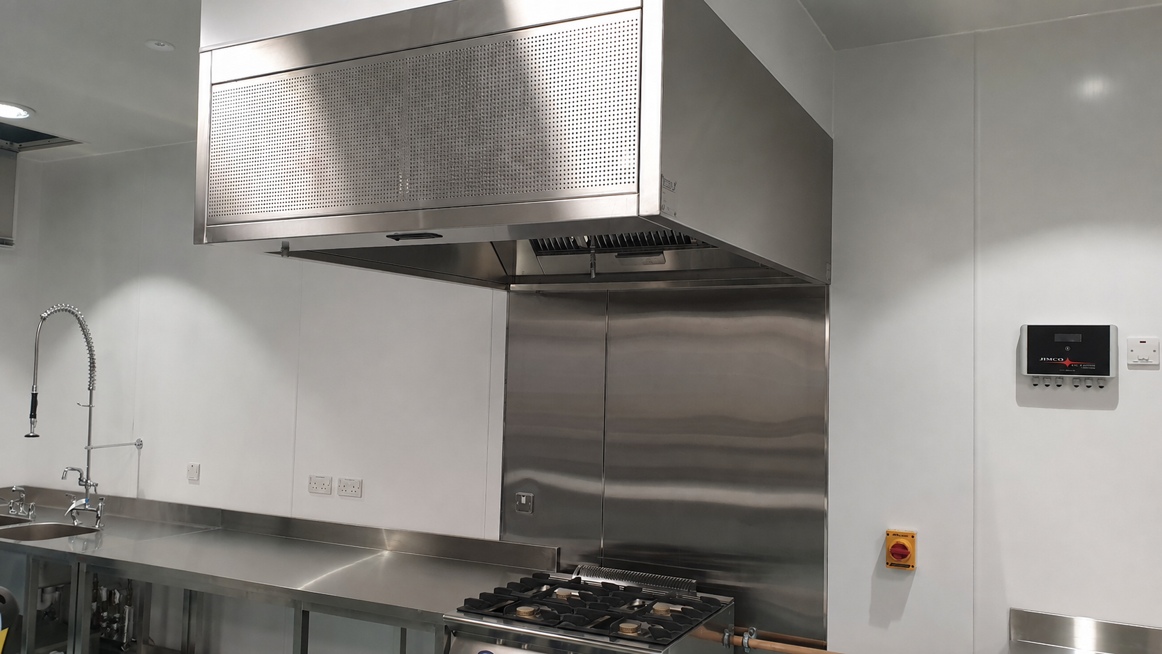 Stainless steel commercial kitchen with range hood, gas stove, sink, and white cabinets