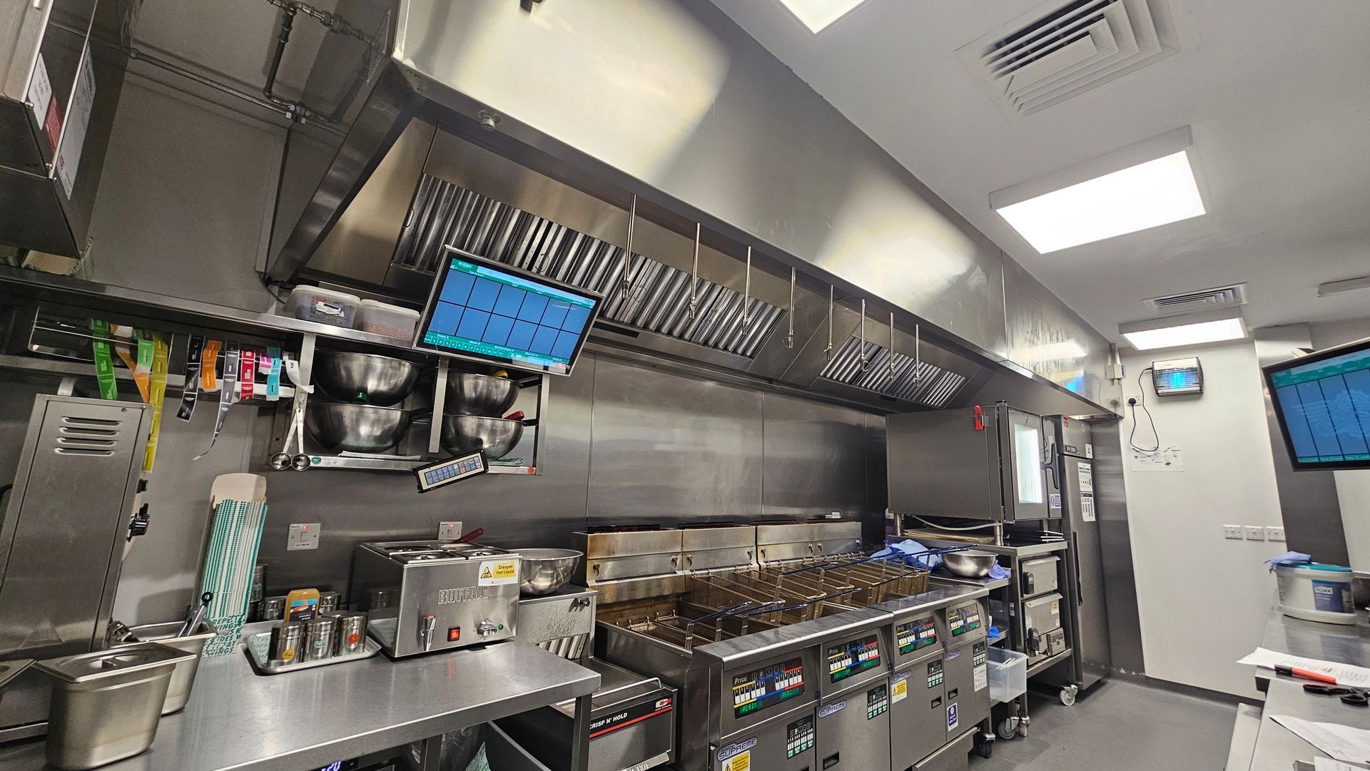 Commercial kitchen with stainless steel counters, hanging utensils, and prep equipment under bright overhead lights