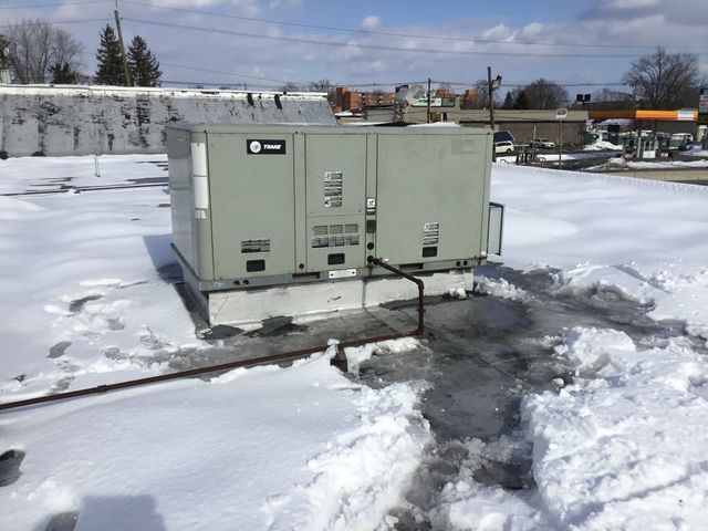 Green industrial generator on a snowy rooftop beside a cleared path