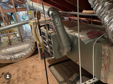 Attic HVAC system with insulated ductwork, metal vents, and foil-wrapped air handler near rafters