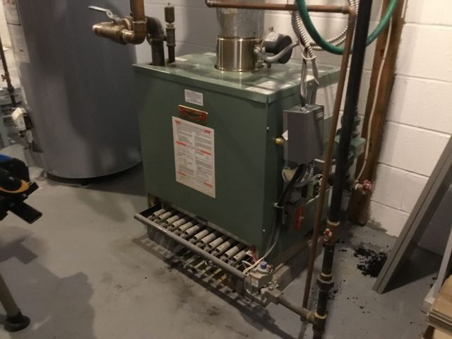 Green industrial boiler in a utility room with exposed pipes and valves on the right.