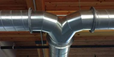 Metal HVAC ductwork with a Y-shaped vent and silver pipes on a ceiling