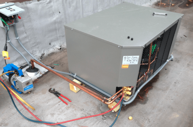Large gray HVAC unit with exposed copper piping and tools on a concrete floor in a work area
