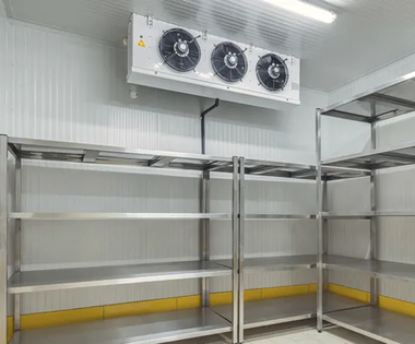 Industrial walk-in cooler interior with stainless steel shelving and wall-mounted refrigeration fans.
