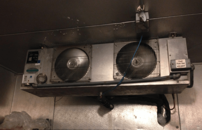 Ceiling-mounted industrial fan unit with two large fans above a metal surface.