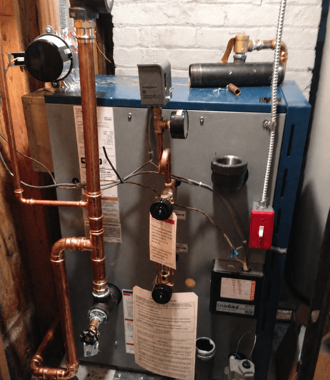 Boiler room equipment with blue and gray furnaces, copper piping, and a red valve lever.