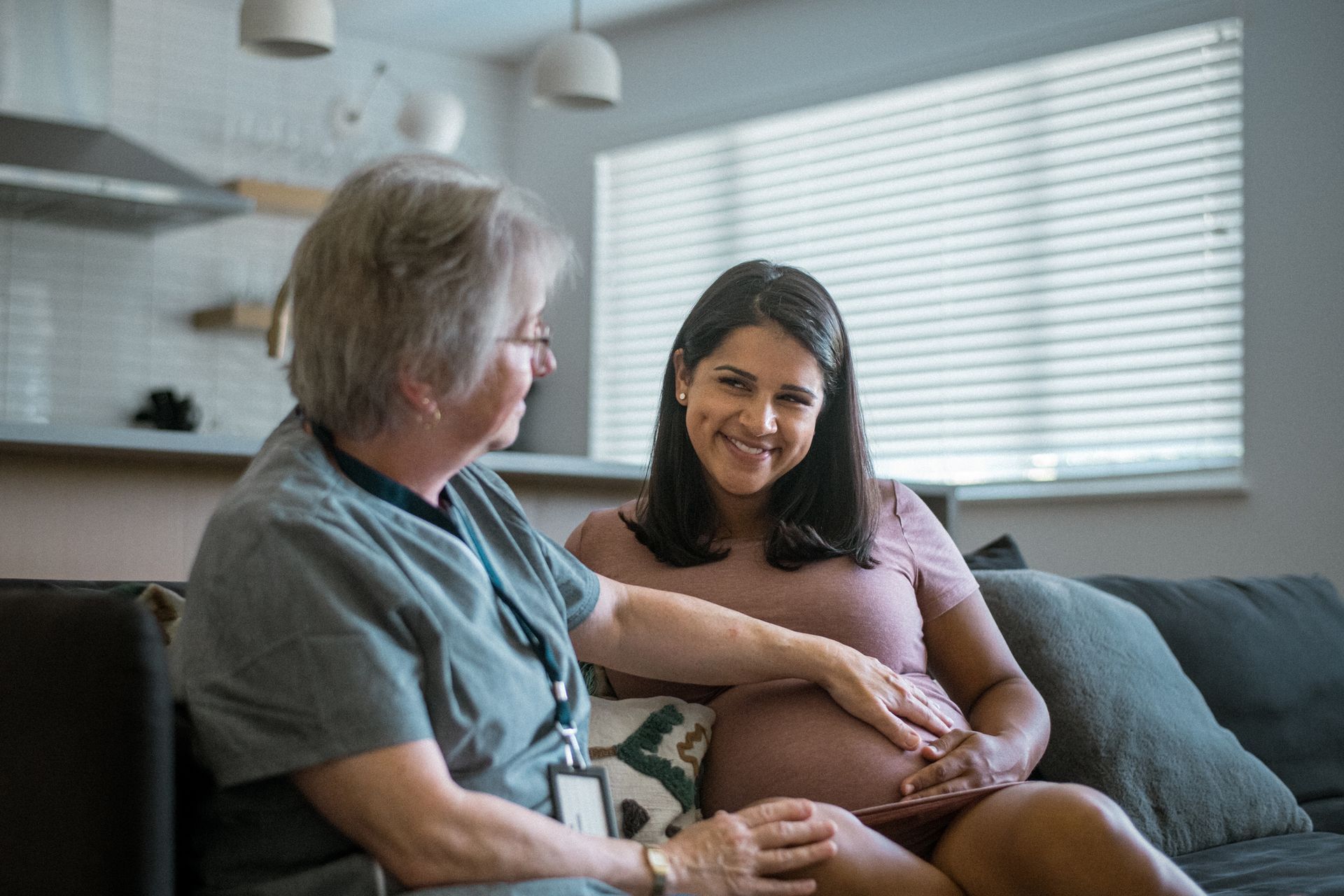 A Pregnant Woman Smiles While a Healthcare Worker Checks Her Belly — Gowen, MI — RiverSong Midwifery