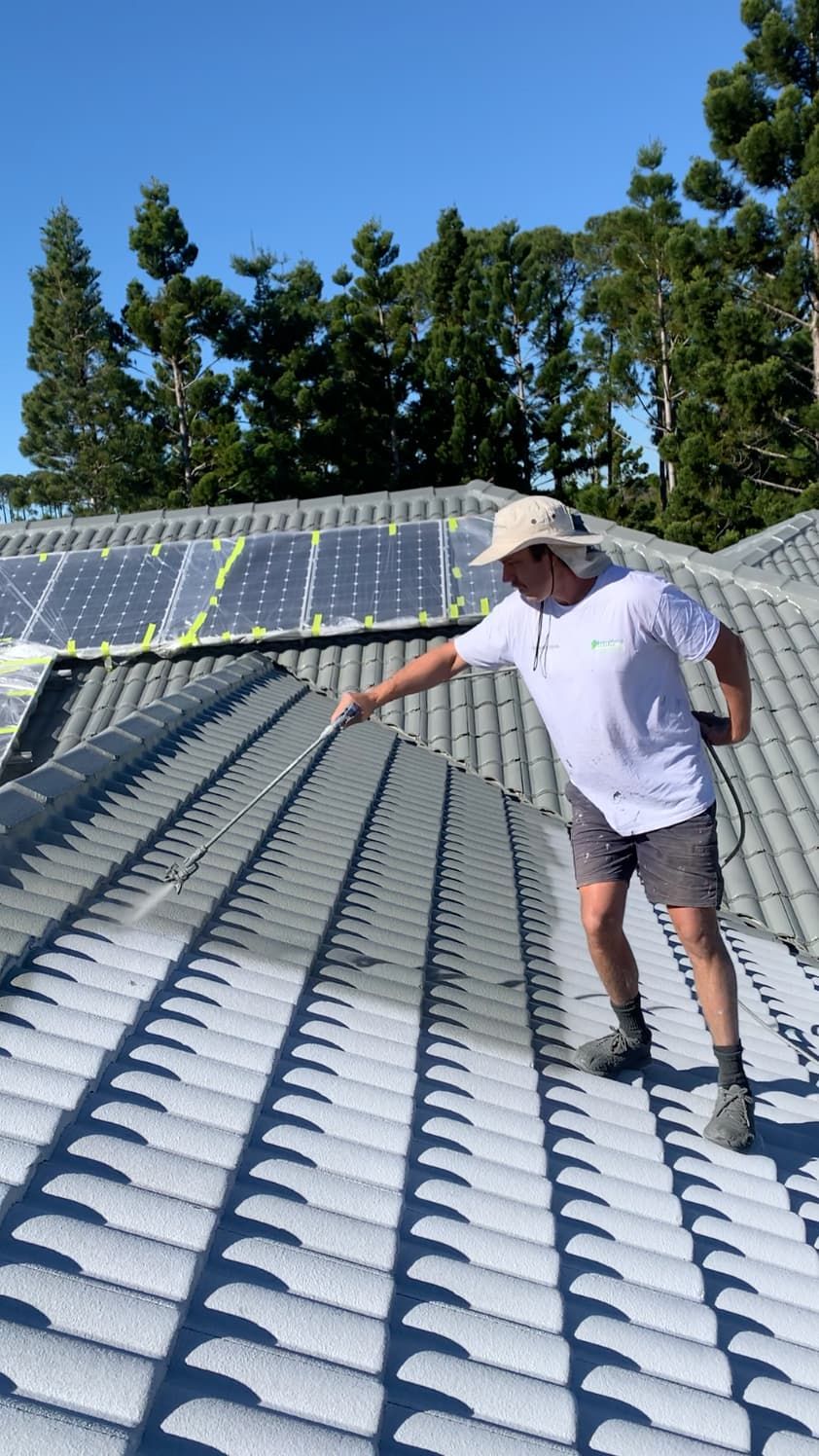 A man is standing on top of a roof painting it.