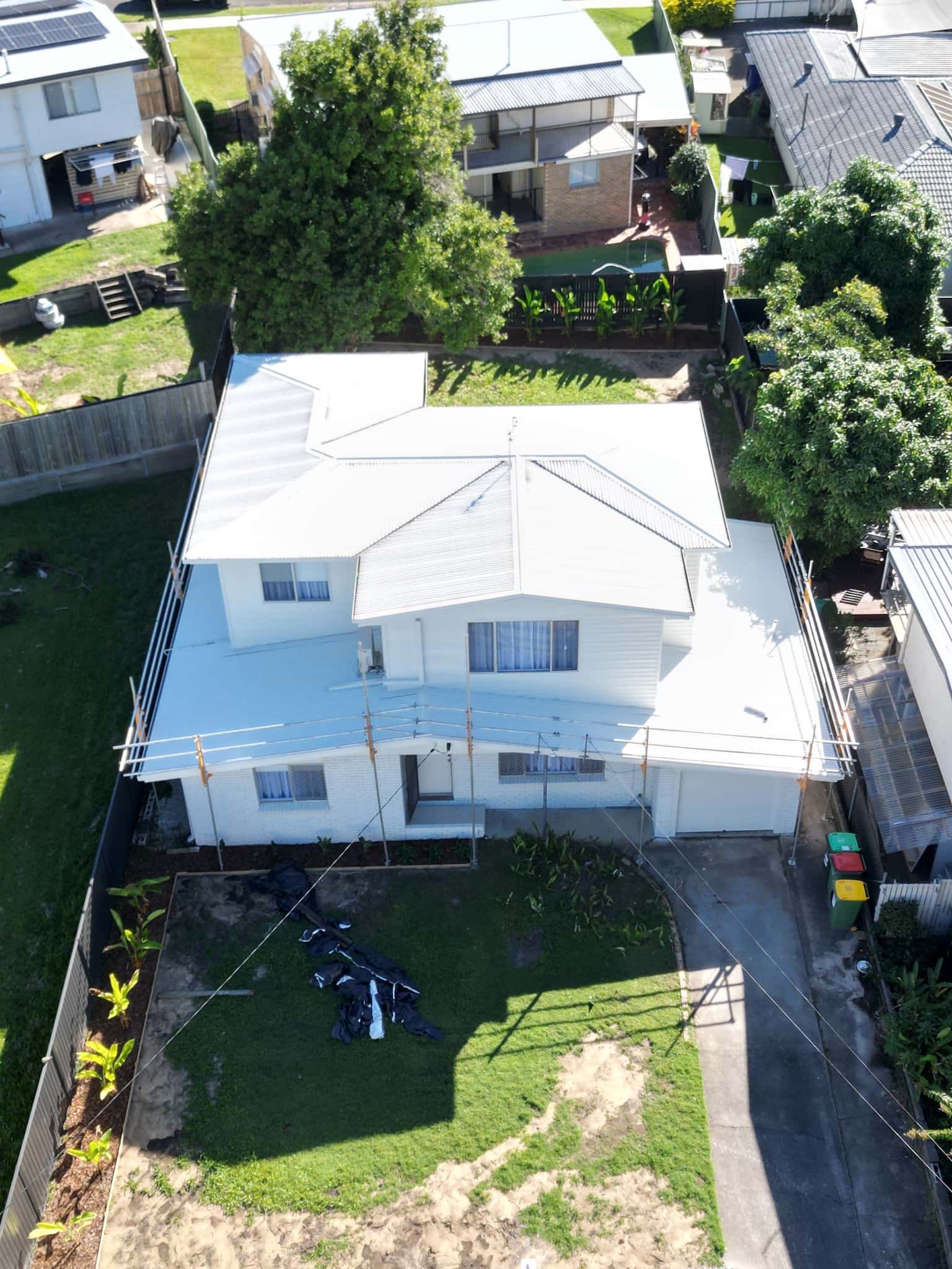 An aerial view of a white, two-story suburban house under construction, surrounded by a lawn and adjacent homes.
