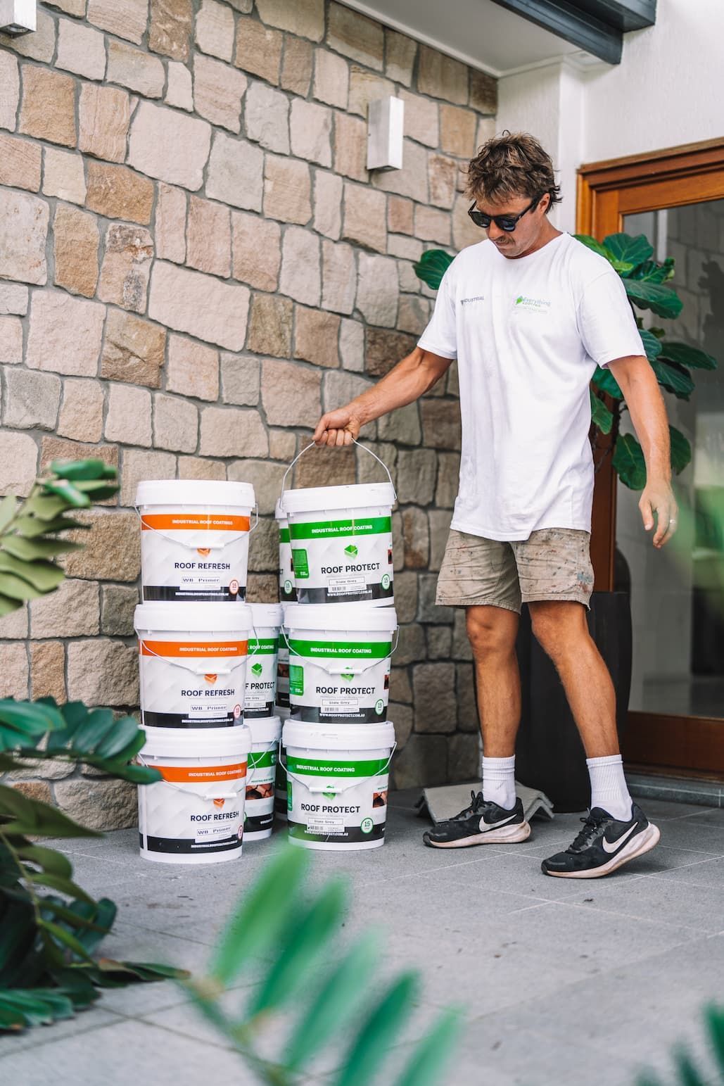 A man is standing next to a stack of buckets of paint.