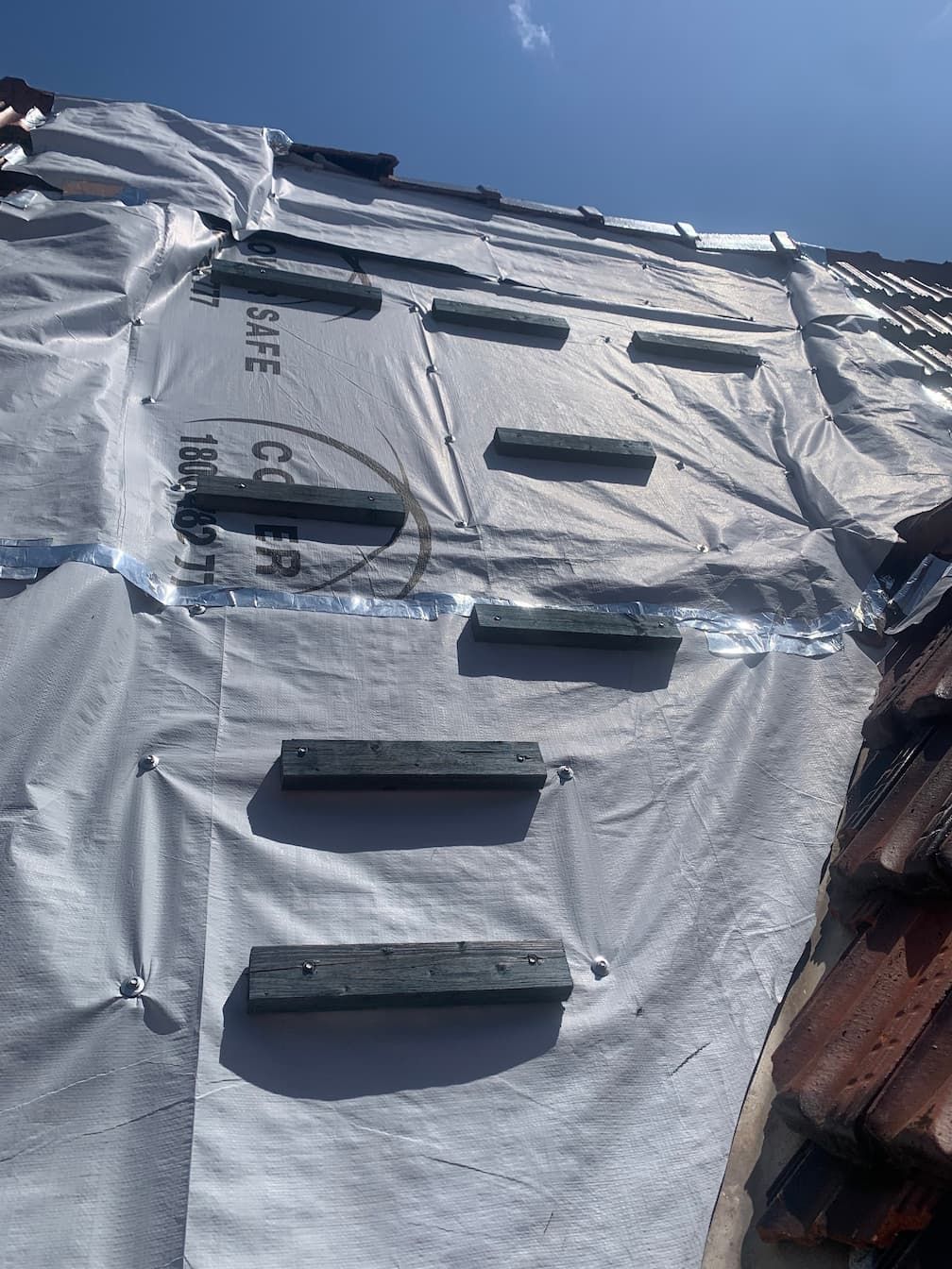 A roof is being covered with a white tarp and wooden steps.