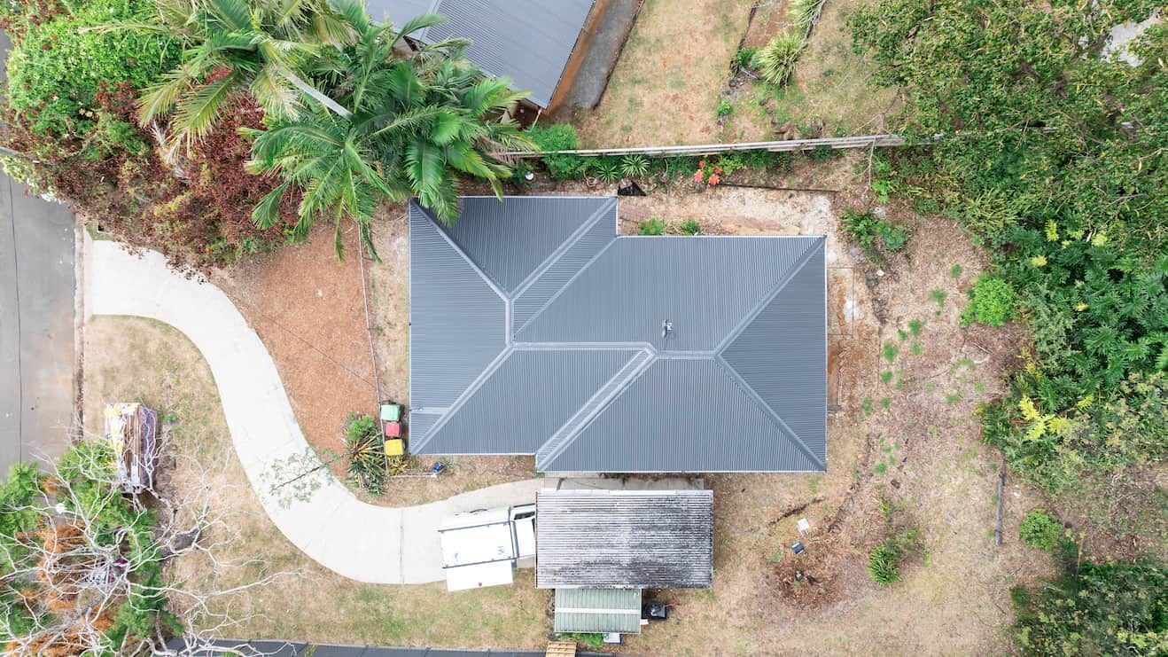 Aerial view of a gray-roofed house with a curved driveway and surrounding trees and yard.