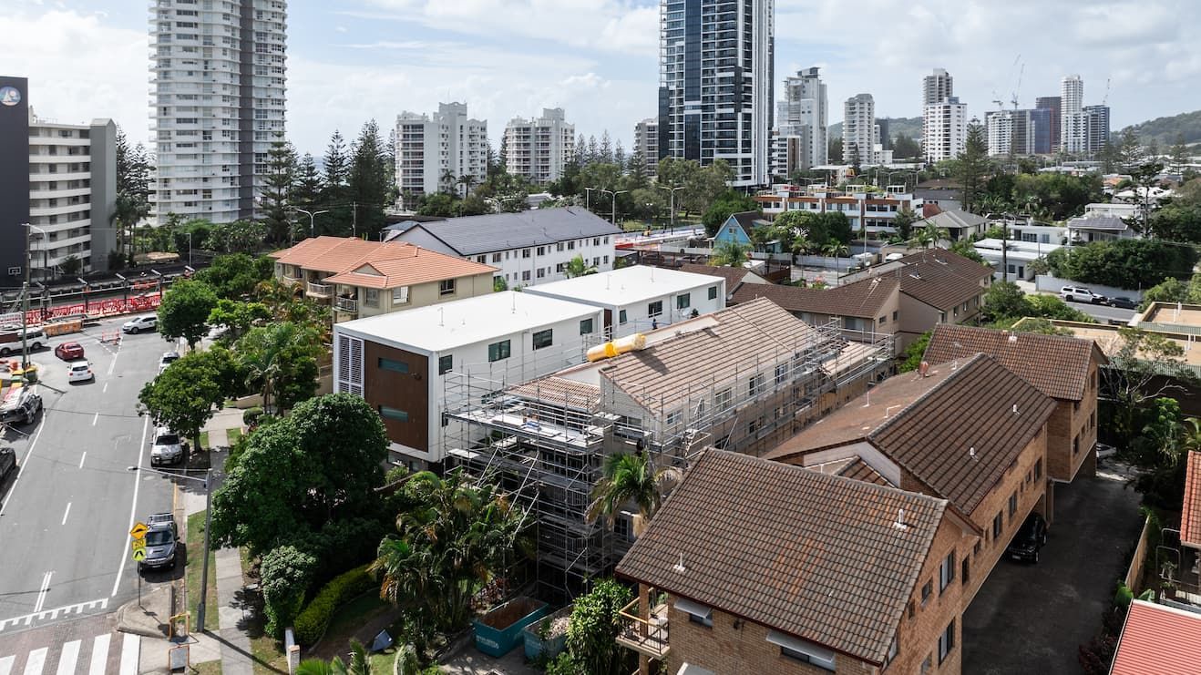 An aerial view shows low-rise residential buildings and construction sites nestled among skyscrapers in an urban setting.