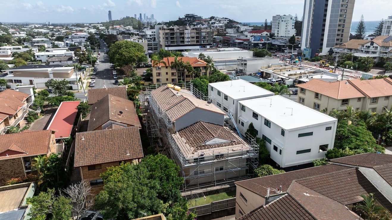 Aerial view of a coastal neighborhood with houses, apartment buildings, and a structure undergoing roof renovations.