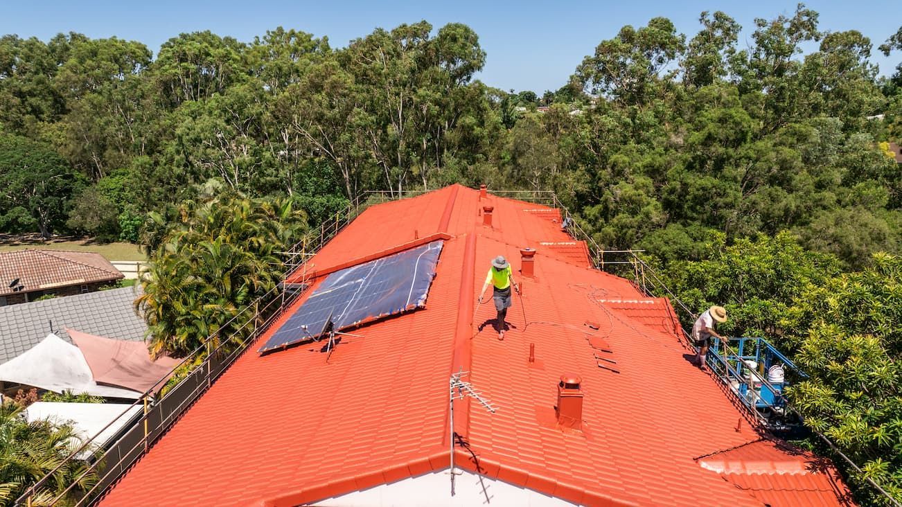 A man is standing on top of a red roof with solar panels on it.