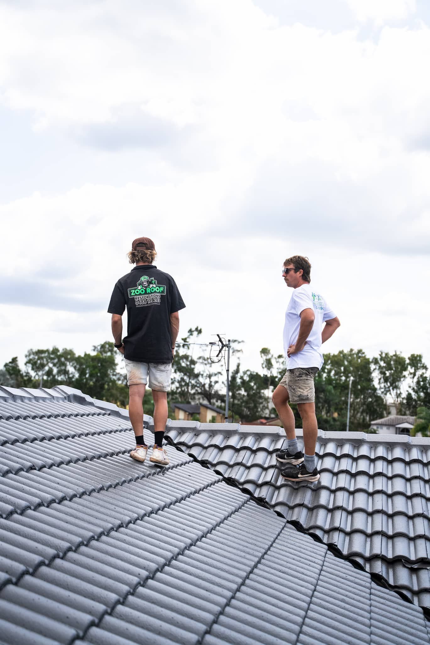 Two men are standing on top of a tiled roof.