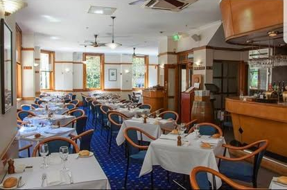 Restaurant dining room with white tablecloths, blue chairs, and a wooden bar.