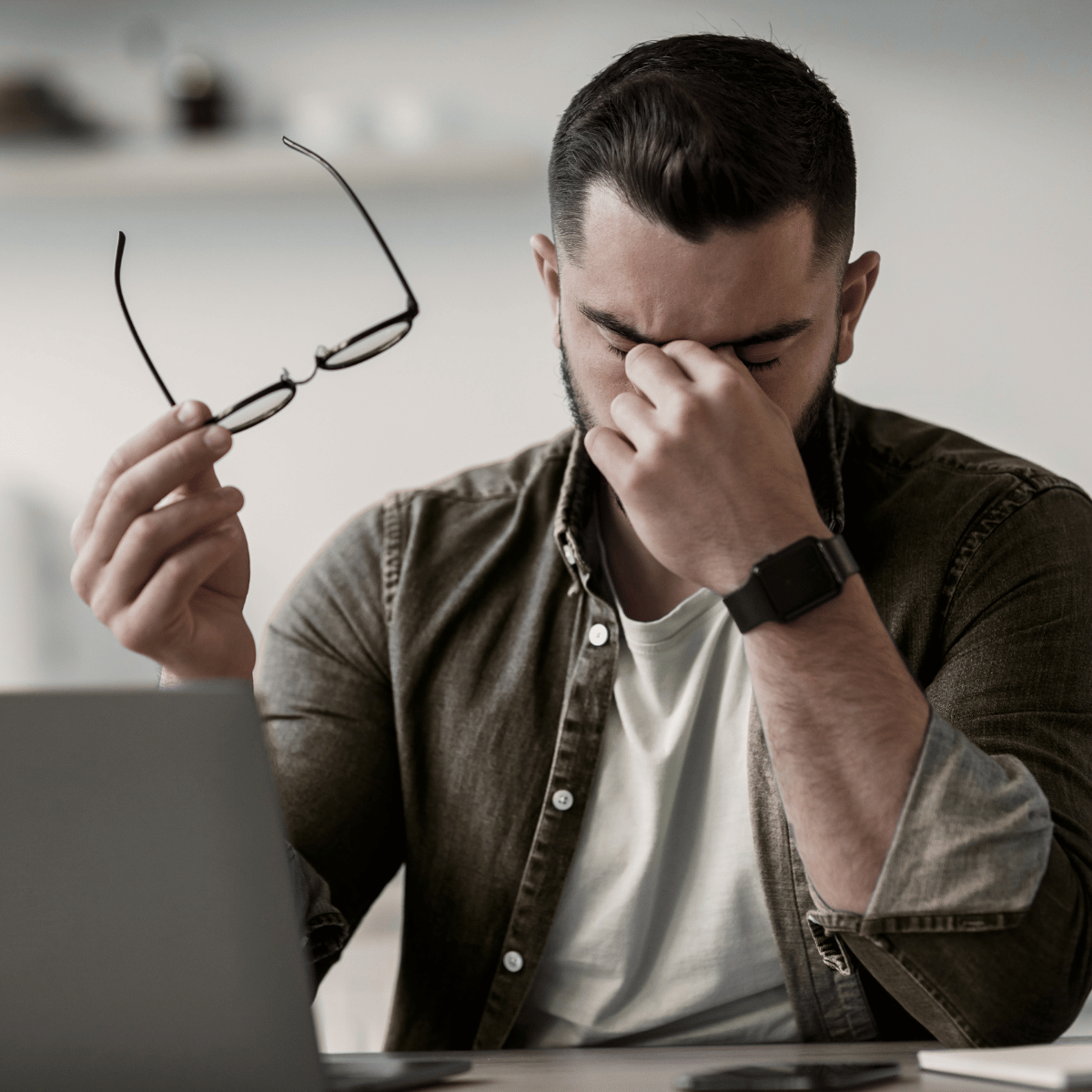 man in front of laptop, rubbing his eyes as though digital eye strain is causing him a headache
