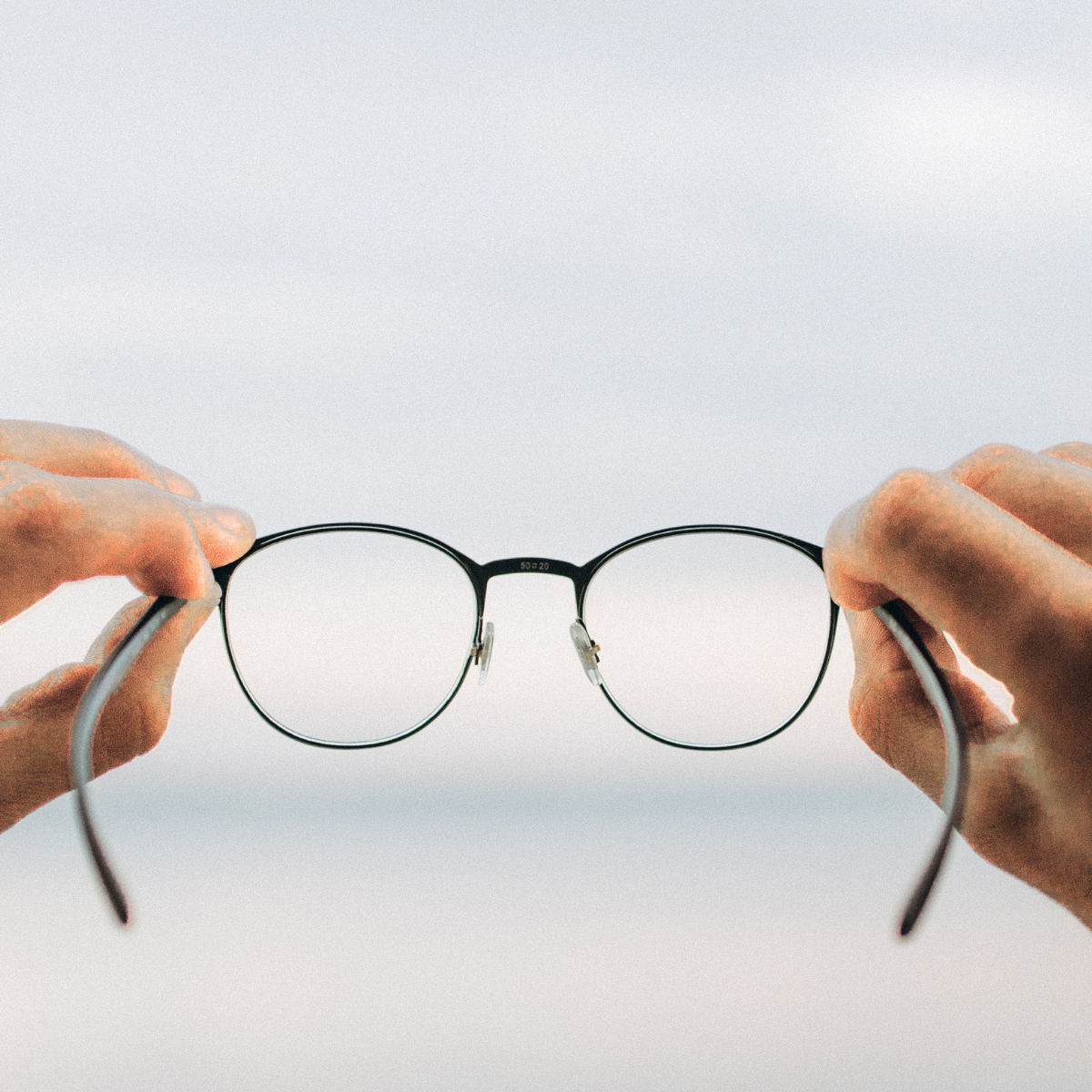 Photo of someone holding up glasses representing Anti Glare Lenses vs. Blue Light Filter