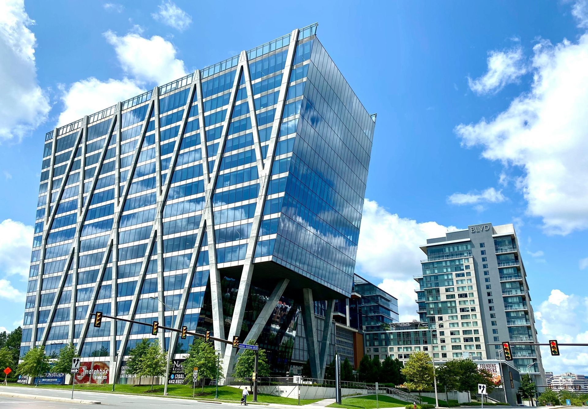 Modern glass and steel office building with unique diagonal support beams, blue sky backdrop.