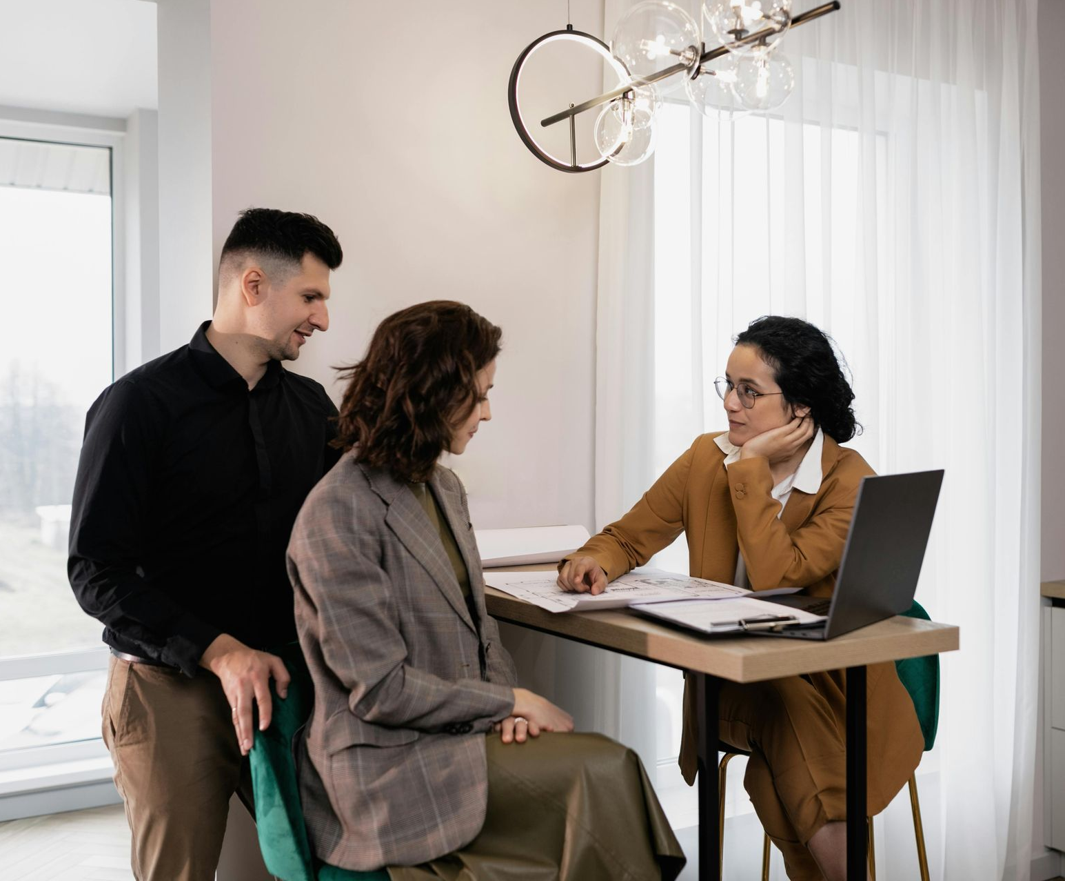 A couple consults with a professional at a desk with paperwork and a laptop.