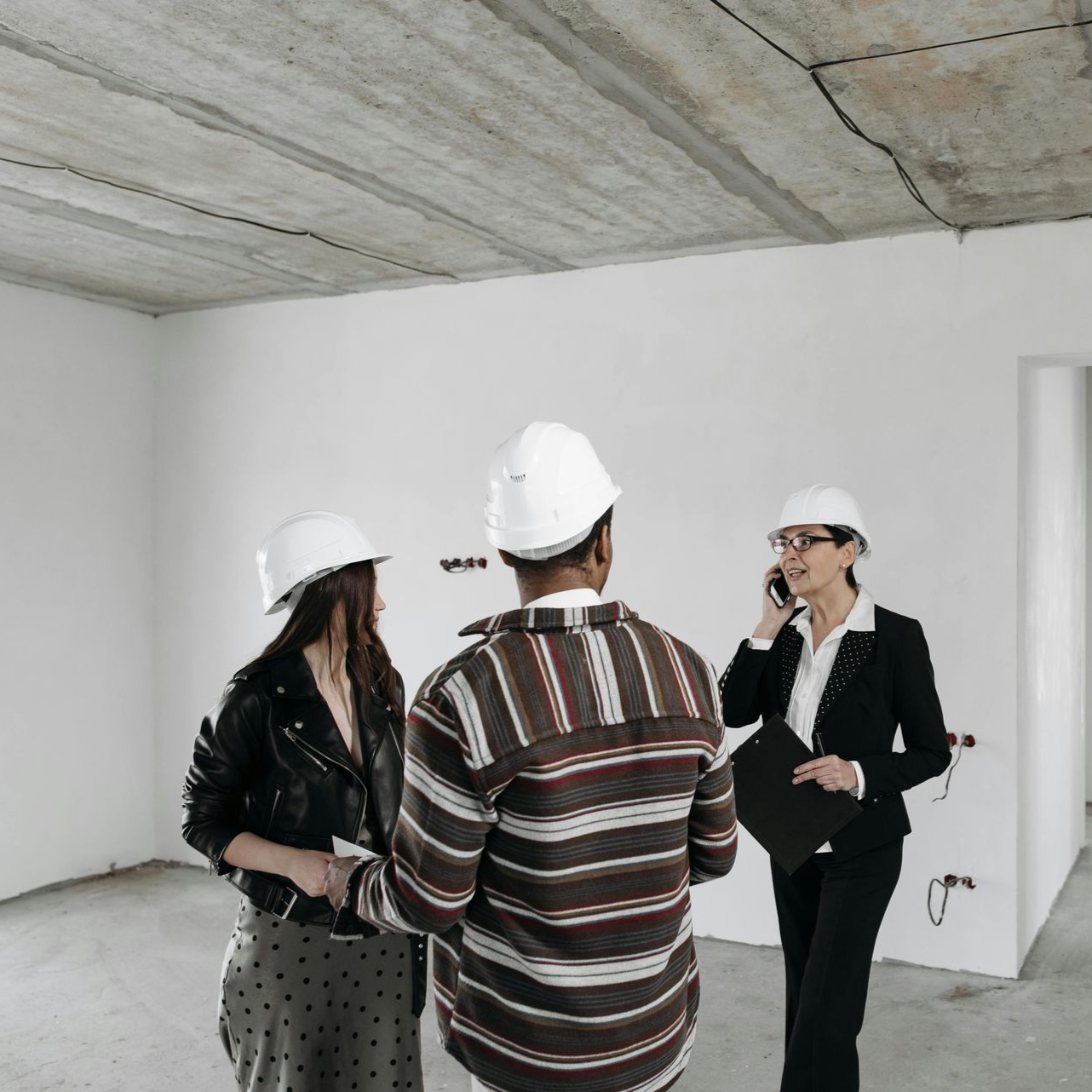 Three people in hard hats inspecting a construction site; one is on a phone, two are conversing.