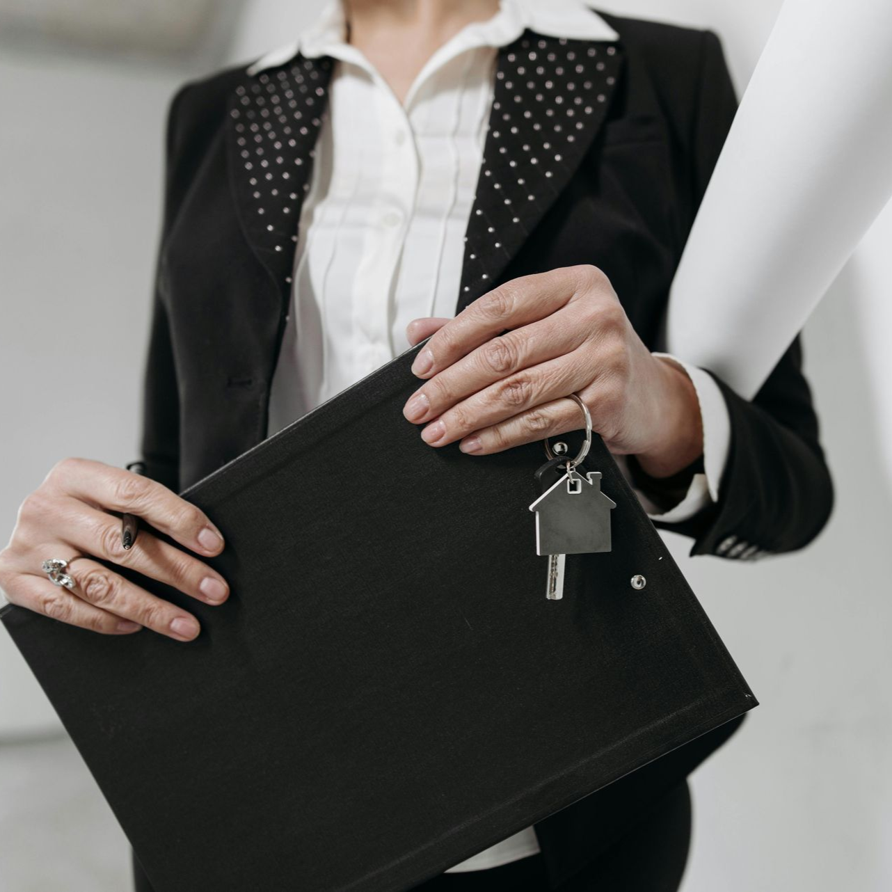 Woman in suit holding a folder with house key and rolled up papers.