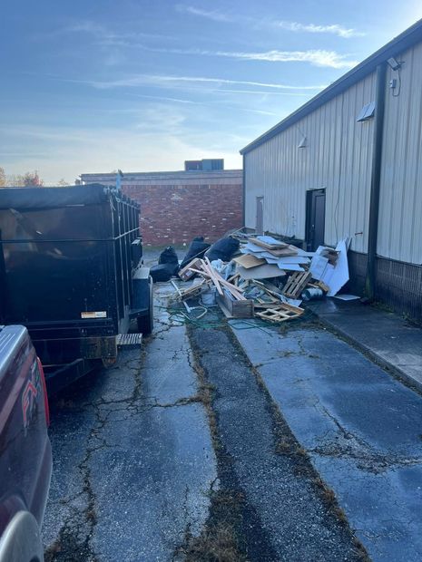 Alley beside a warehouse with piles of debris and a dumpster under a blue sky.