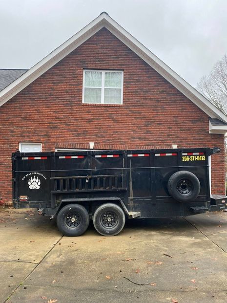 Black dump trailer parked on a driveway in front of a brick house.