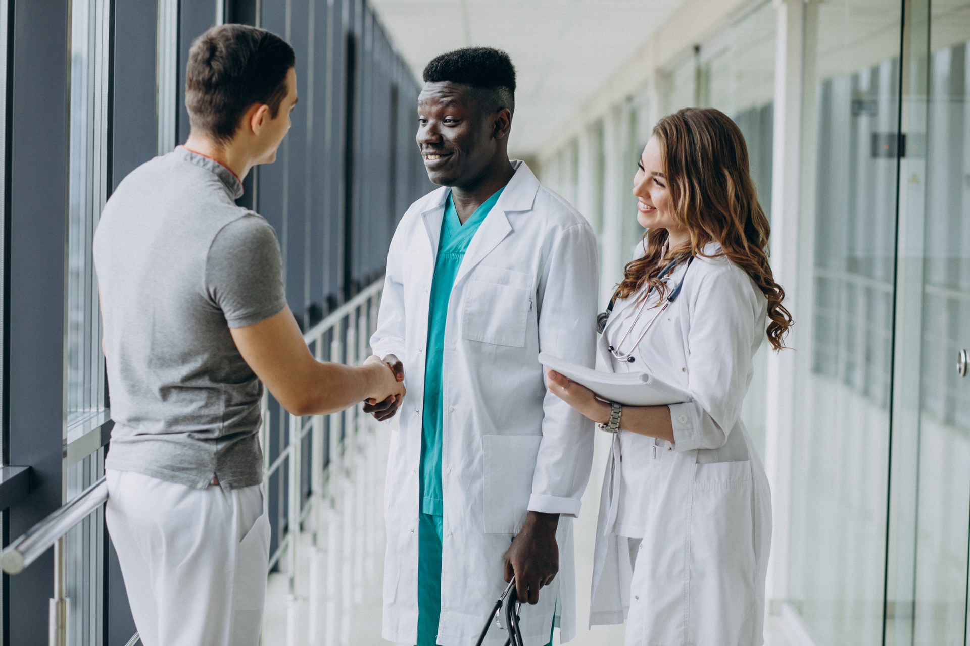 A male doctor shaking hands with a patient while another healthcare worker stands by his side.