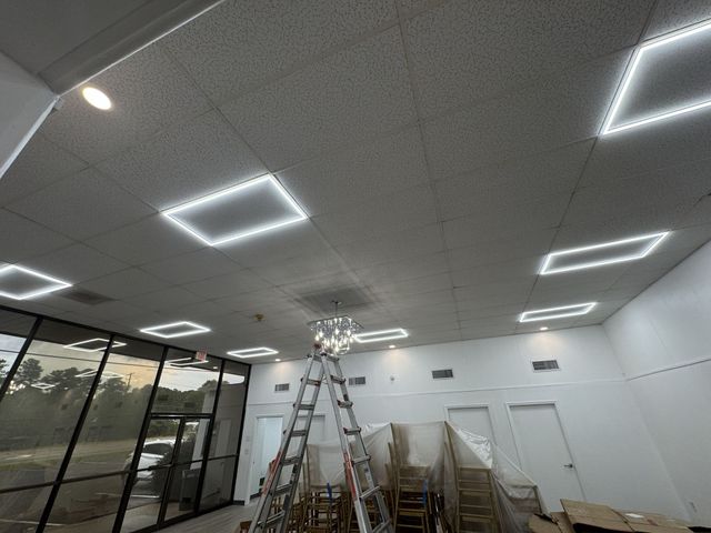 Empty room with ladders, stacked chairs, and bright square ceiling lights during setup or renovation