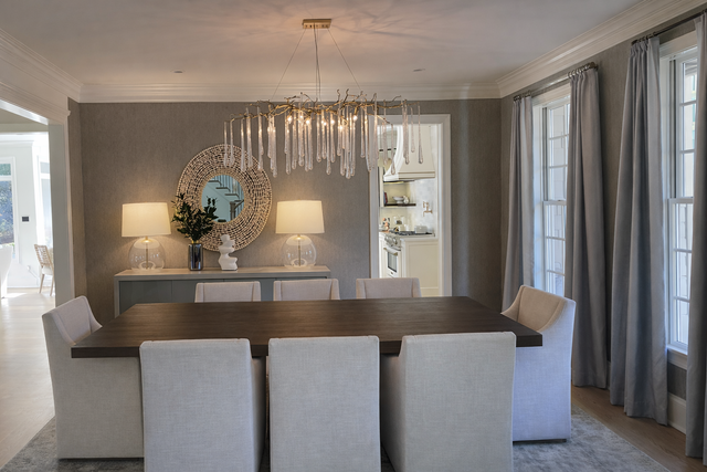 Bright dining room with a glass chandelier, neutral chairs, and a mirrored sideboard beside tall windows