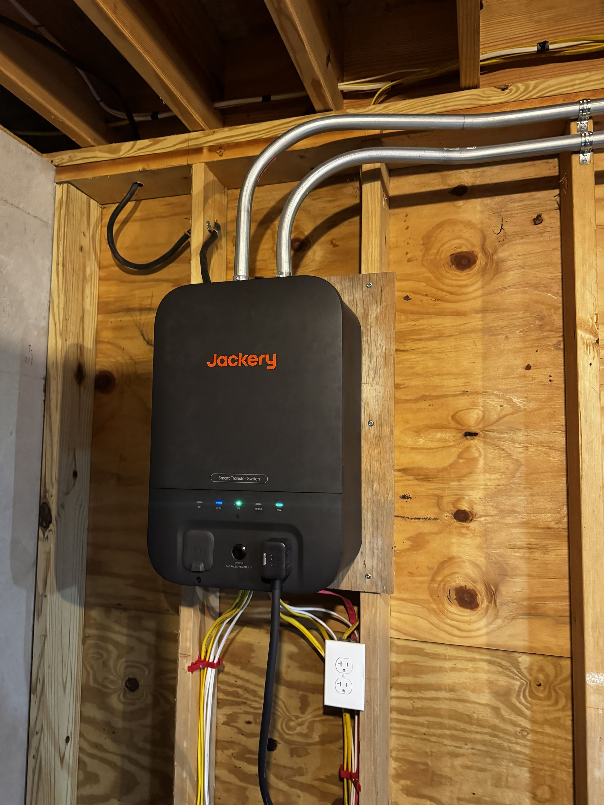 JACKERY battery backup mounted on plywood wall with electrical conduits and exposed ceiling joists