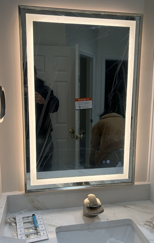 Bathroom mirror with lit LED frame reflecting two people and a door in the background
