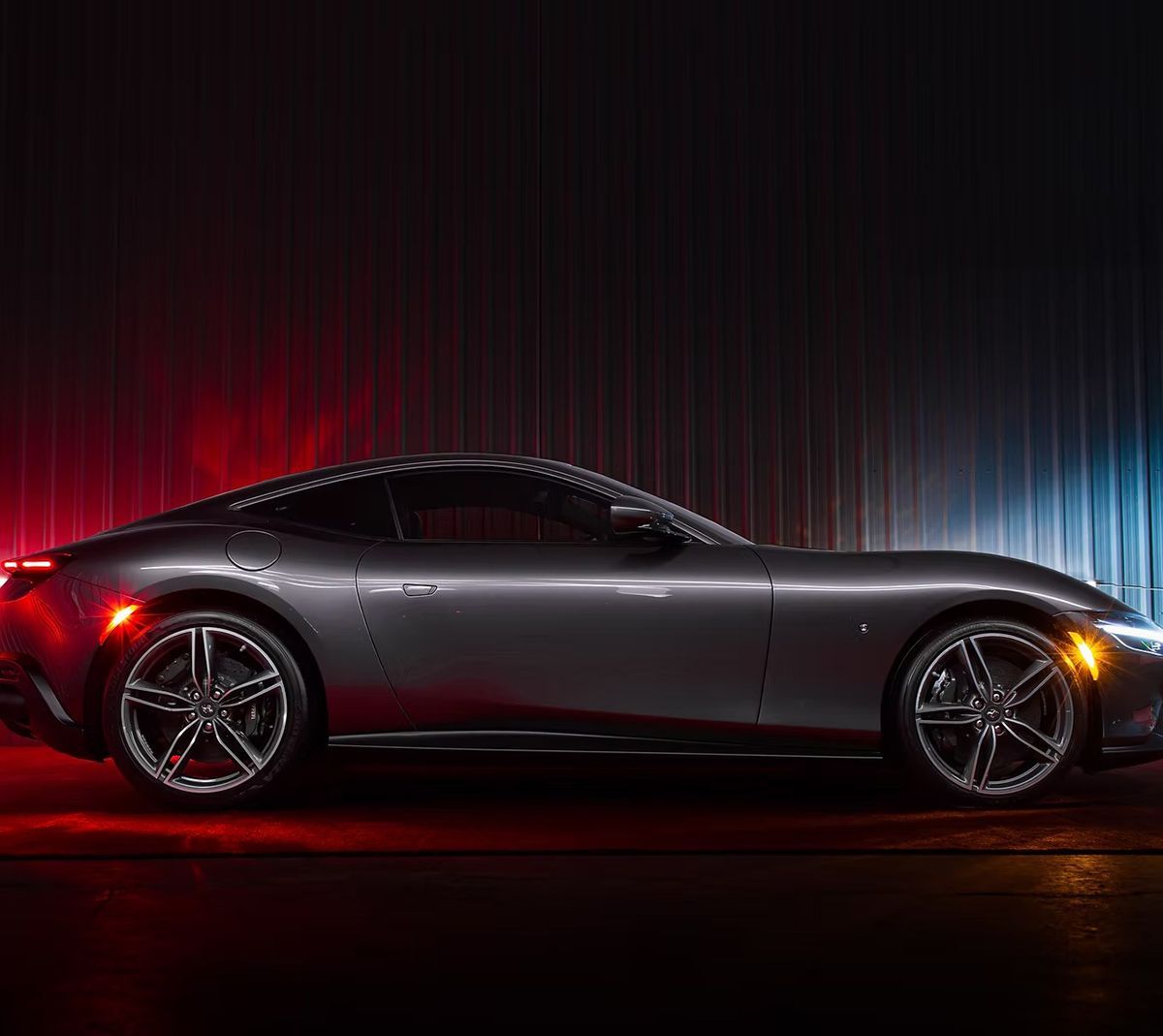 Gray Ferrari sports car in dark setting with red and blue lighting.