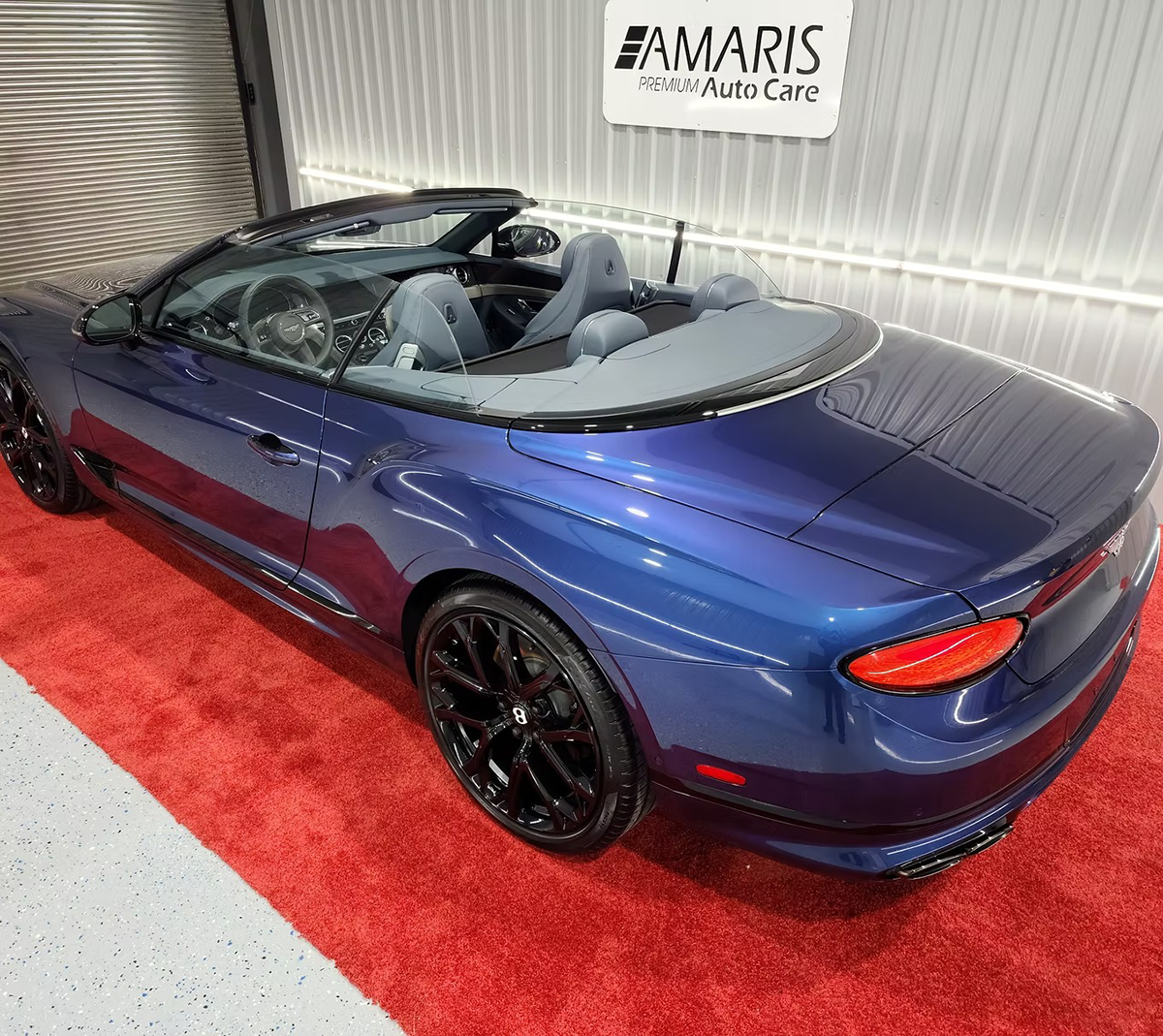 Blue convertible car with black wheels, parked on a red carpet. 