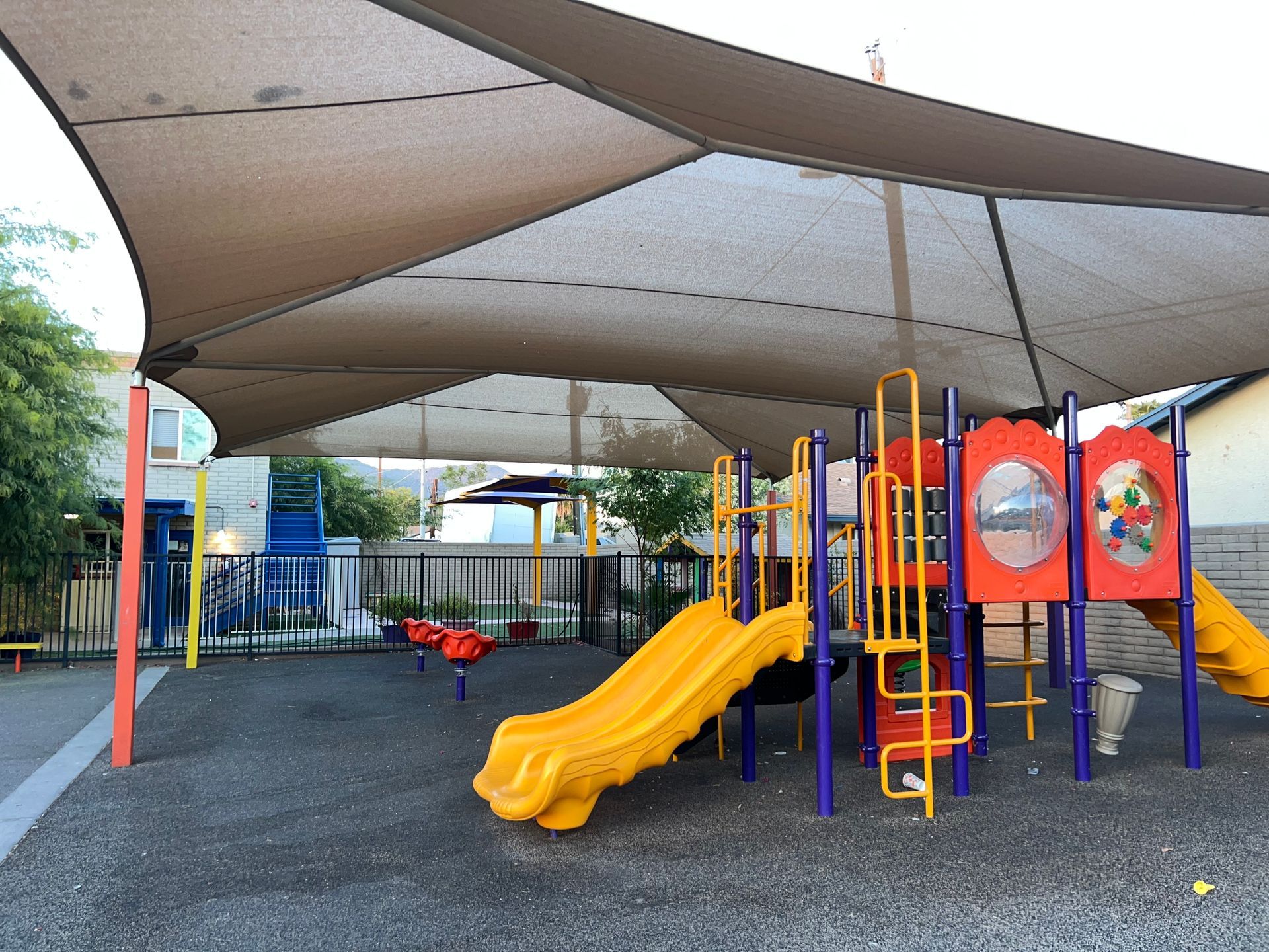 Playground with a shade structure. Yellow slides and climbing structures.
